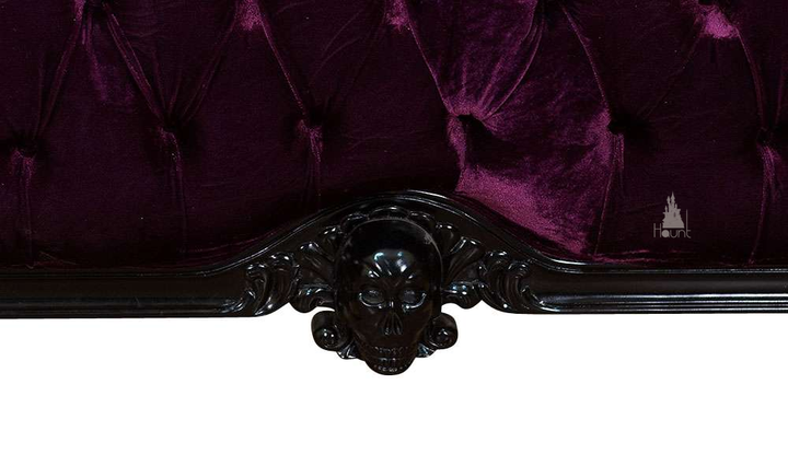The Death Aphrodite Bed, a handcrafted upholstered gothic bed with a tall shaped headboard, curved footboard and a carved skull crest.